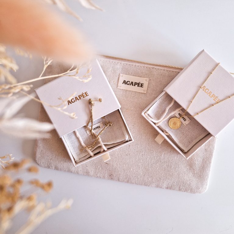 Agapée : Des bijoux durables inspirés de la Méditerranée Collier Alba et boucles d’oreilles Grazia de la marque de bijoux Agapée dans leur écrin en carton recyclé, posés sur la pochette en coton et lin