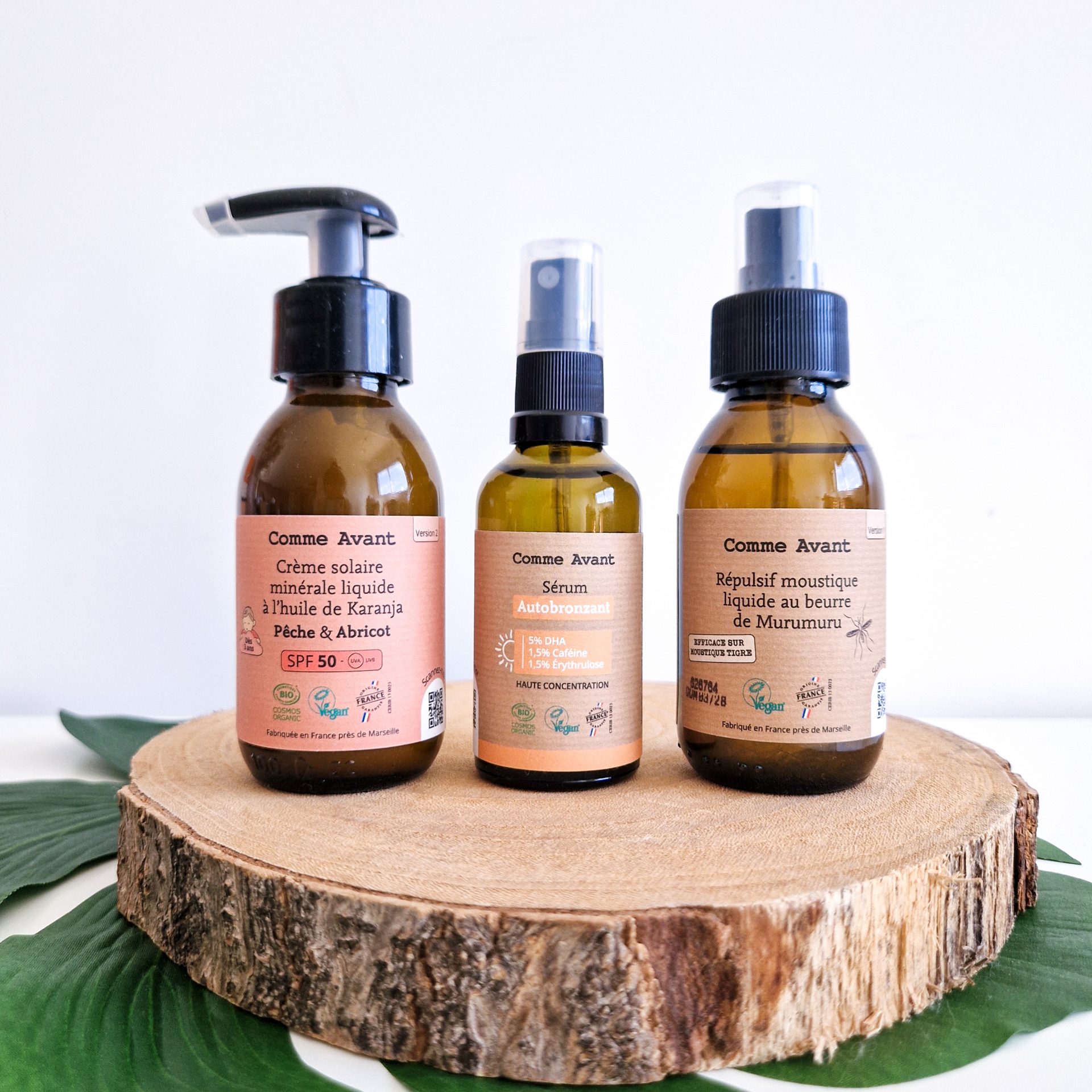 Crème solaire, autobronzant et anti-moustique Comme Avant : mes 3 indispensables de l’été Crème solaire minérale, sérum autobronzant et répulsif anti-moustique liquide Comme Avant posés côte à côte sur une rondelle de bois